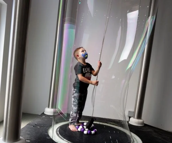 Visitor inside a giant soap bubble at the Bubble Monster exhibit