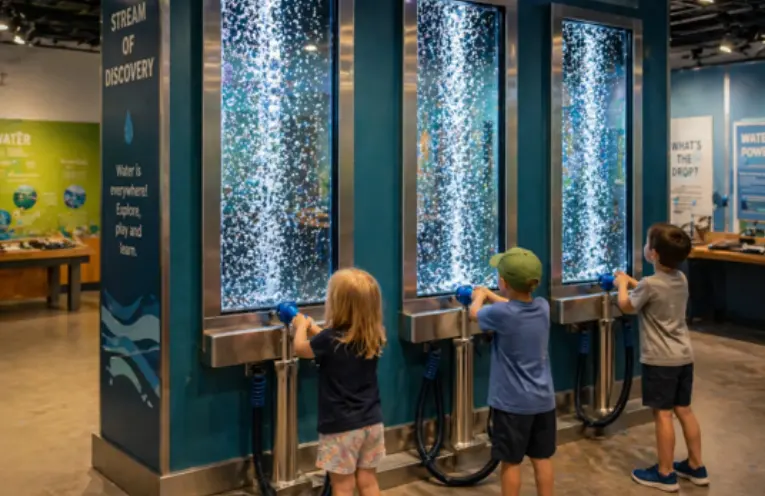 Children pumping air into tall illuminated bubble columns at the Pump The Bubbles exhibit