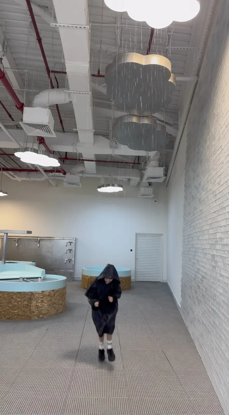 Visitor standing beneath the falling rain of the Raining Clouds exhibit