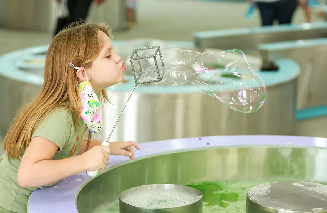 Child blowing a giant bubble with a cube-shaped wand